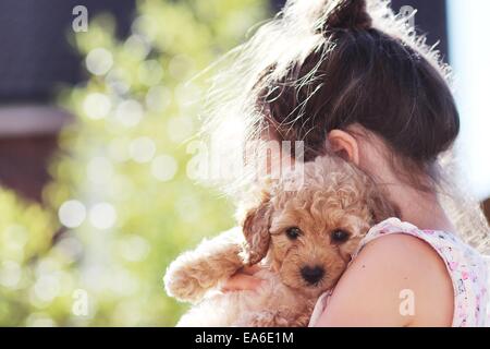 Giovane ragazza in piedi nel giardino coccolando il suo cane cucciolo Foto Stock