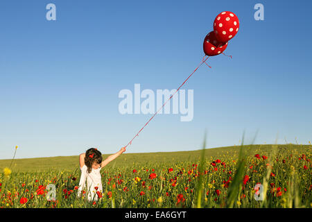 Ragazza in piedi in un campo di fiori di papavero azienda polka dot palloncini Foto Stock