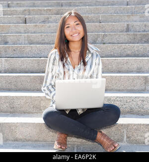 Bella ragazza asiatica seduta sulle scale e utilizzando un computer portatile Foto Stock