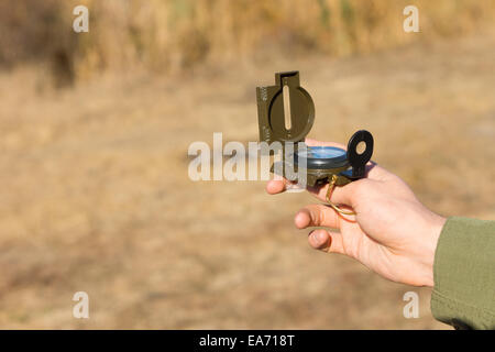 Giovane uomo in possesso di una bussola magnetica come egli sta all'aperto nella campagna di utilizzarlo per la navigazione e per trovare la sua geographic Foto Stock