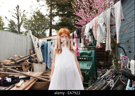 Ritratto di ragazza gingerhead (8-9) indossando abito bianco in piedi nel cortile disseminato Foto Stock