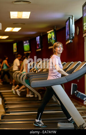 Donna matura camminando sul tapis roulant della palestra Foto Stock