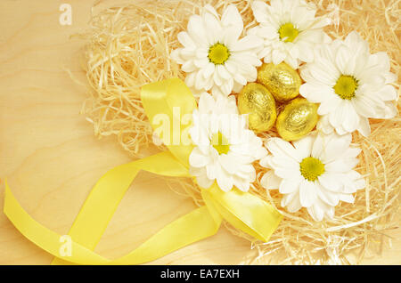 Golden uova e fiori nel nido su un sfondo di legno per la Pasqua Foto Stock