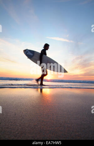 Basso angolo vista del surfista con la tavola da surf a piedi lungo il bordo delle acque durante il tramonto Constantine Bay vicino a Padstow North Cornwall Sout Foto Stock