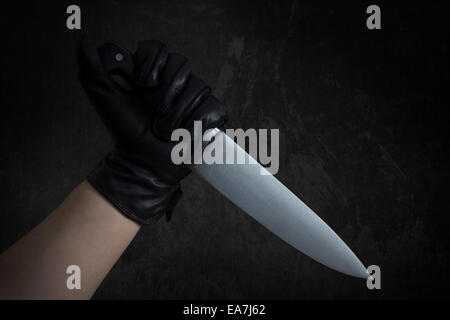 Un braccio con guanti neri in pelle tenendo un coltello di grandi dimensioni Foto Stock