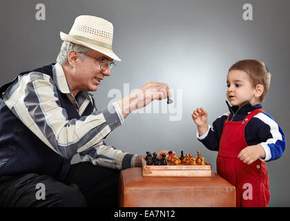 Il nonno e nipote a giocare una partita a scacchi su sfondo grigio Foto Stock