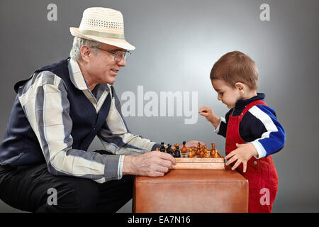 Il nonno e nipote a giocare una partita a scacchi su sfondo grigio Foto Stock