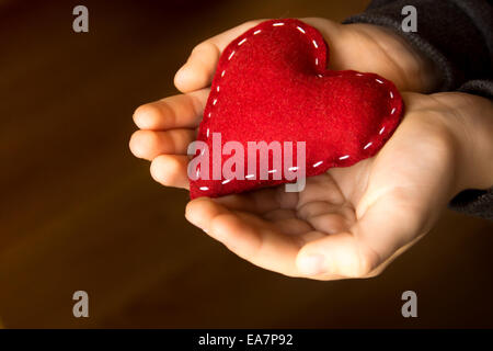 Cuore rosso nelle mani del bambino, fatto a mano regalo, il giorno di San Valentino e amore familiare concetto, close up, orizzontale Foto Stock