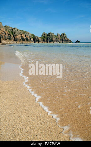 Waters Edge increspature sulla spiaggia Treen accanto alla spiaggia di Porthcurno a bassa marea con vista sulla baia di Treryn Dinas & Logan Rock Pe Foto Stock