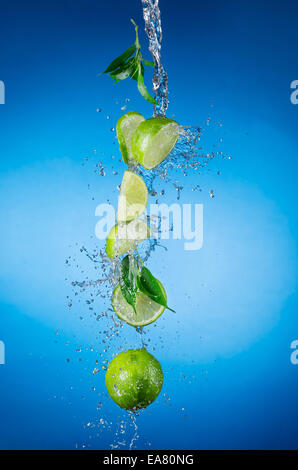 Studio shot di Limette fresche con acqua splash su sfondo blu Foto Stock