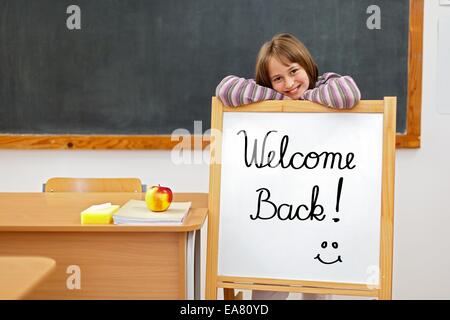 School girl in aula, dietro un pannello con Welcome Back script Foto Stock