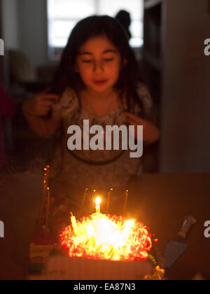 Giovane ragazza a casa soffiando fuori candele su una torta di compleanno. Foto Stock