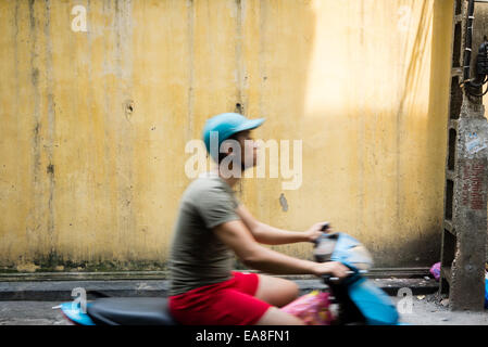 Uomo che cavalca scooter passato parete gialla nella città vecchia di Hanoi e Foto Stock