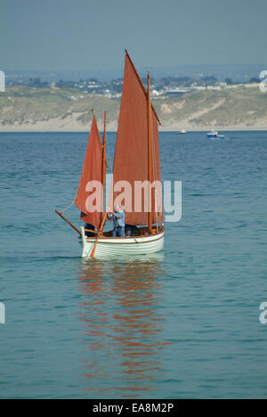 Bianco marrone mondati navigato Lugger vela in St Ives Bay con uomo con remo per spostare la barca su una calma estati nebuloso Penwith di pomeriggio Foto Stock
