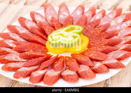 Salsicce fresche e i peperoni in piastra sul tappetino di bambù sfondo. Foto Stock