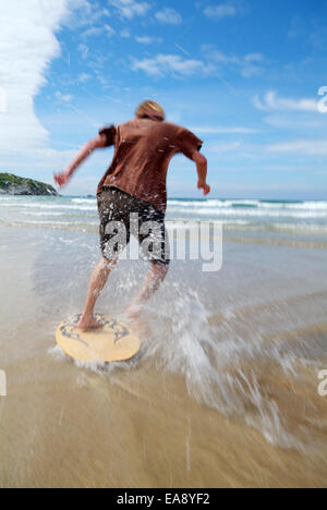 Giovane uomo scrematura a bordo lungo il bordo delle acque a bassa marea sulla spiaggia a Newquay sulla North Cornish Coast Restormel metà Cornw Foto Stock