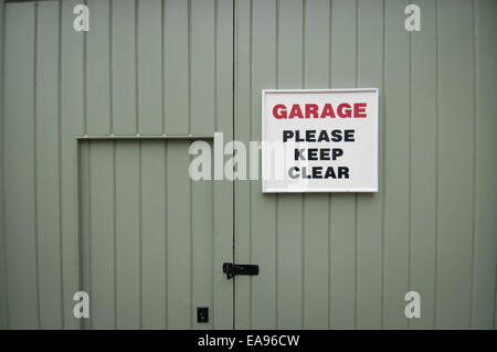 Porta di Garage dipinte di verde con un segno dicendo 'garage si prega di tenere sgombra l' Foto Stock