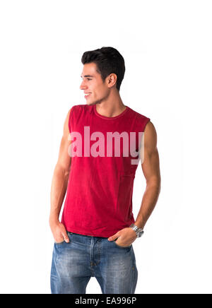 Attraente sorridente giovane uomo in rosso maglia senza maniche e jeans, guardando ad un lato in corrispondenza di uno spazio vuoto accanto a lui, isolato su bianco Foto Stock