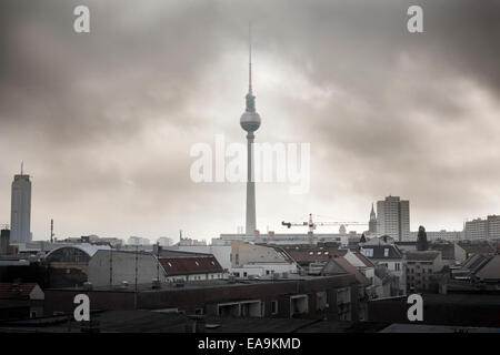 Fernsehturm Berlin TV Tower attraverso i tetti della città di Berlino su un nuvoloso giorno grigio con blocchi a torre, appartamenti e alloggi e una gru Foto Stock