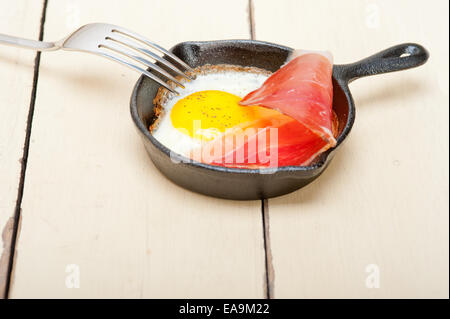 Uovo fritto sunny side up italiana con speck prosciutto affumicato su una padella Foto Stock