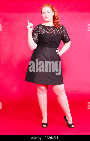 I giovani i capelli rossi chubby donna in un abito nero e look di poppa. Foto Stock