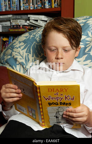 Schoolboy a casa leggendo Diario di un Wimpy Kid Dog Days libro Foto Stock