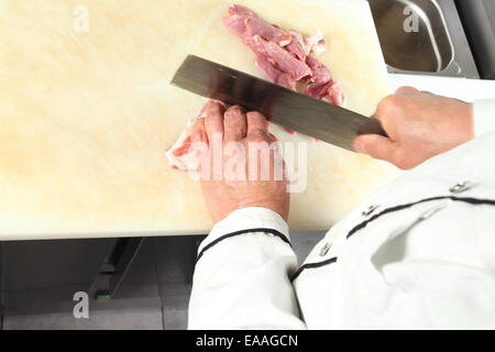 Un Cuoco il taglio di materie soddisfare con coltello di grosse dimensioni Foto Stock