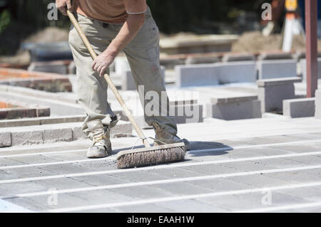 Un uomo con un pennello su un pavimento di cemento in un cantiere. Foto Stock