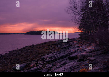 Guardando oltre una spiaggia rocciosa di un tramonto, area tra orizzonte nubi e illuminato con forte rosa-luce arancione Foto Stock