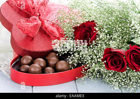 Cuore scatola sagomata di San Valentino di cioccolatini con belle gambo lungo rose rosse. Foto Stock