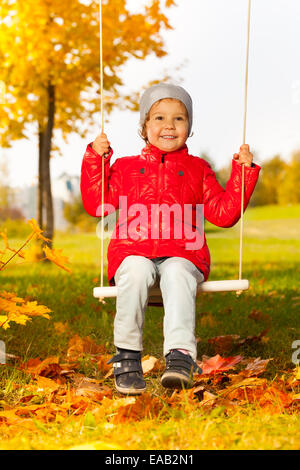 Felice ragazza siede su altalene e sorrisi allegramente Foto Stock