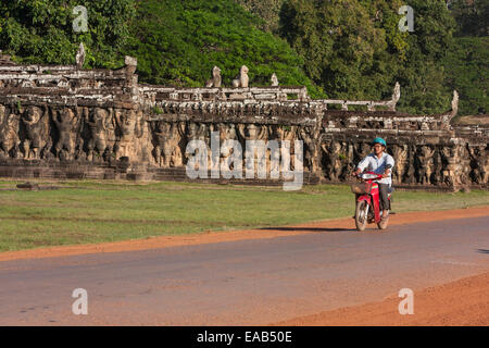 Cambogia Angkor Thom. Uomo sulla bici del motore andando oltre la terrazza dell'Elefante. Foto Stock