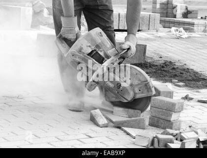 Immagine in bianco e nero di lavoratore con calcestruzzo ha visto nelle sue mani e lavorando in condizioni polverose Foto Stock