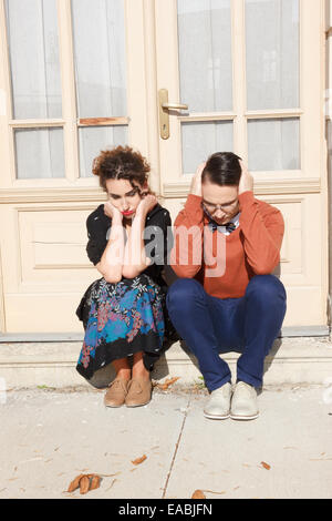 Premuto e agitato l uomo e la donna accovacciata davanti alla casa di scale a causa problema hanno, triste emozioni Foto Stock