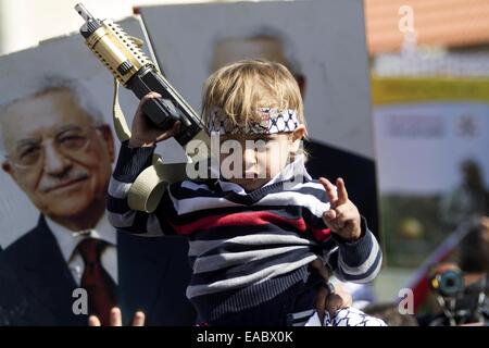 Ramallah, West Bank, Territorio palestinese. Decimo Nov, 2014. Un ragazzo palestinese lampeggia un segno di vittoria durante un rally per celebrare il decimo anniversario della morte del tardo leader palestinese Yasser Arafat in Cisgiordania città di Ramallah il 11 novembre 2014. Arafat è morto in un ospedale militare vicino a Parigi il 11 novembre 2004 in circostanze che non sono mai state chiare e due anni fa, di esperti svizzeri che hanno esaminato i suoi effetti personali riportati trovare ''anomalo "" livelli di polonio, estremamente tossina radioattivi, alimentando la diffusa convinzione palestinese che era stato avvelenato da Israele. Il Jewi Foto Stock