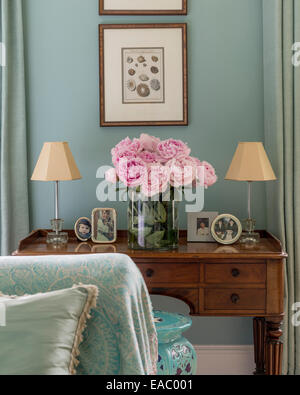 Peonie rosa antico sul tavolo con le foto incorniciate e piccole lampade Foto Stock