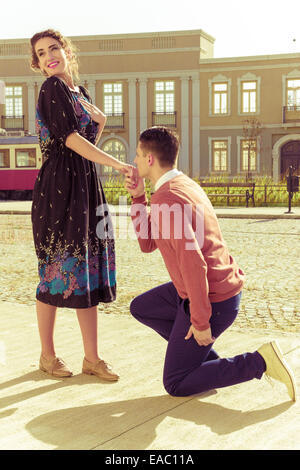 Retro Vintage giovane uomo in ginocchio e chiedendo una ragazza di sposare lui nel parco sul marciapiede , a piedi con affetto e pasion com Foto Stock