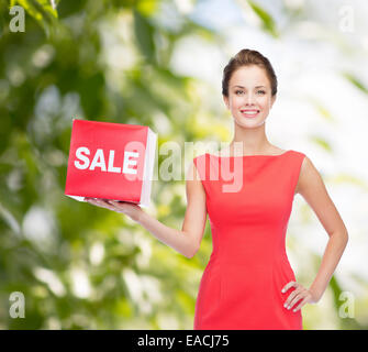 Sorridente giovane donna in abito rosso con segno di vendita Foto Stock