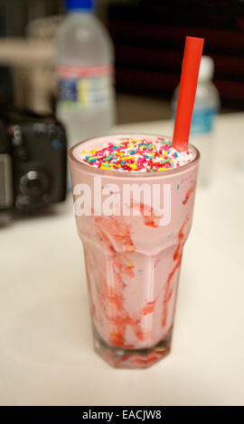 Bicchiere riempito con il frullato fragole con colore rosso brillante e paglia con bottiglia di acqua debolmente visibile in background Foto Stock