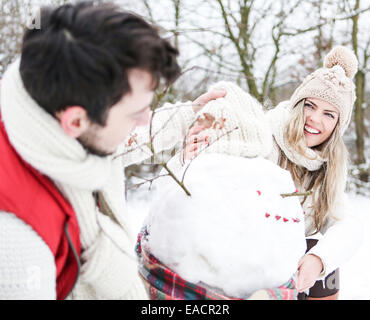 Coppia felice costruire un pupazzo di neve insieme in inverno Foto Stock