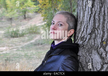 La donna in nero appoggiato su di un tronco di albero nella foresta di autunno Foto Stock