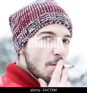 Giovane uomo con berretto di lana di fumare sigarette in inverno Foto Stock