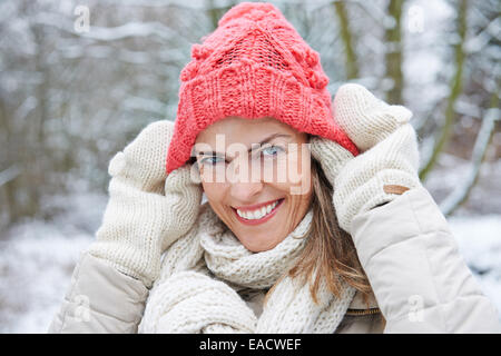 Donna sorridente in inverno lana mettendo il cappello sulla sua testa Foto Stock