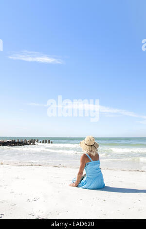 Donna matura seduto sulla spiaggia Coquina, Anna Maria Island, Florida Foto Stock