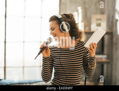 Felice giovane donna cantare karaoke in appartamento loft Foto Stock