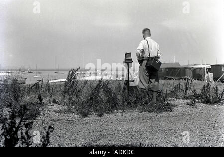 1930s, foto storiche di un fotografo maschio utilizzando un film di grandi dimensioni telecamera box dell'era su un treppiede di legno per scattare una foto della costa di Norfolk. Foto Stock