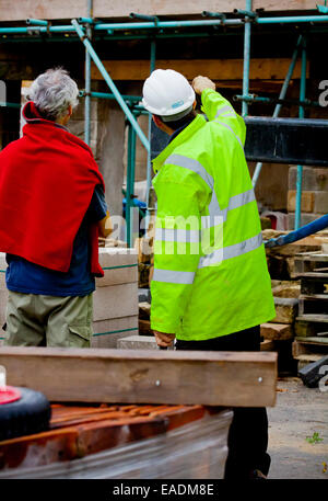 Builder e architetto lavora in un cantiere che indossa un giubbetto alta visibilita e bianco elmetto casco di protezione Foto Stock