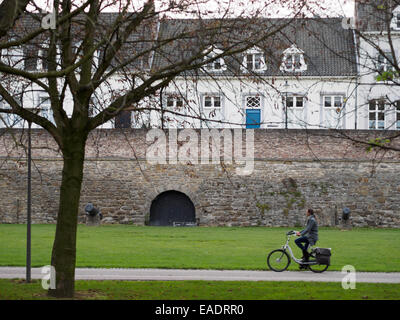 Vista di profilo di una giovane donna in sella ad una bicicletta accanto alle mura della città vecchia di Maastricht, Olanda, Europa Foto Stock