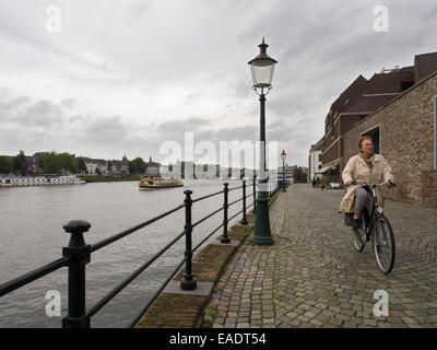 Old Lady in sella ad una bicicletta su una strada a ciottoli accanto al fiume Maas a Maastricht, Olanda, Europa Foto Stock