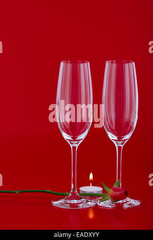 Due bicchieri di vino con rose e candela su sfondo rosso Foto Stock